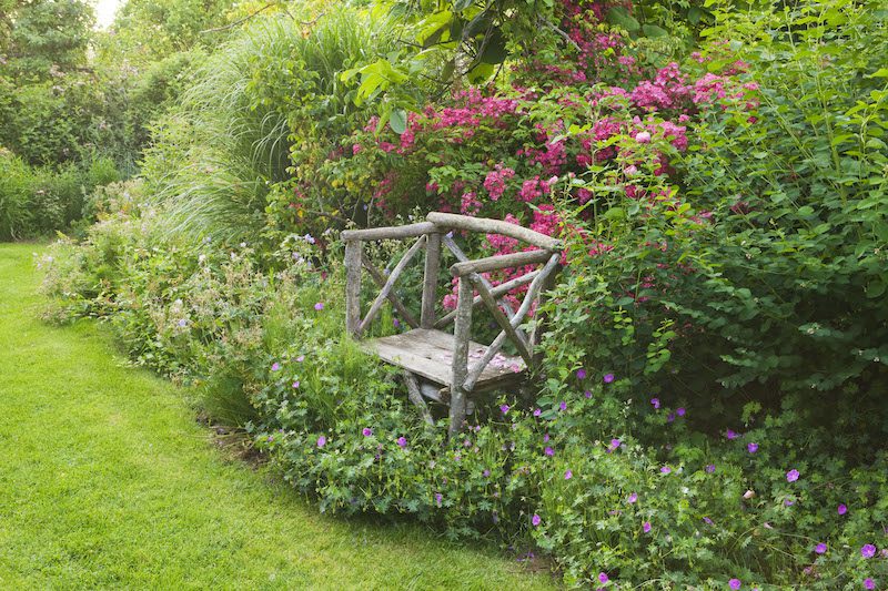 a handmade wooden bench positioned in between flowers in a garden