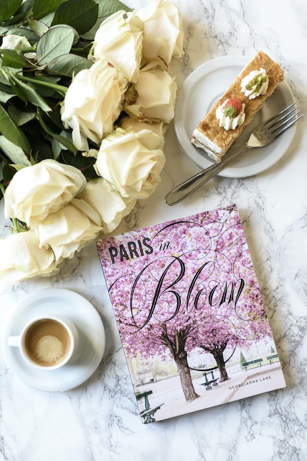 a copy of paris in bloom by georgianna lane on a table with a coffee and yellow roses