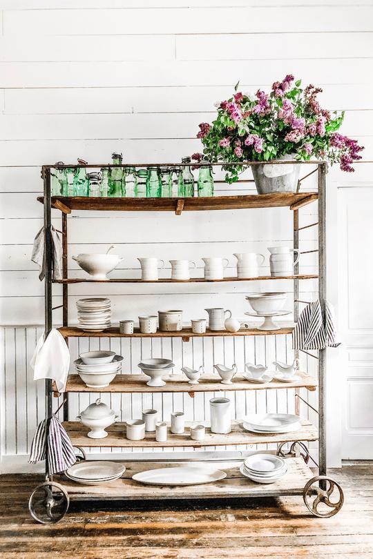 bar cart with white stoneware, green vases and a bouquet of flowers