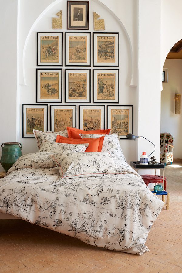 toile de jouy bedspread on bed with orange pillows in front of gallery wall