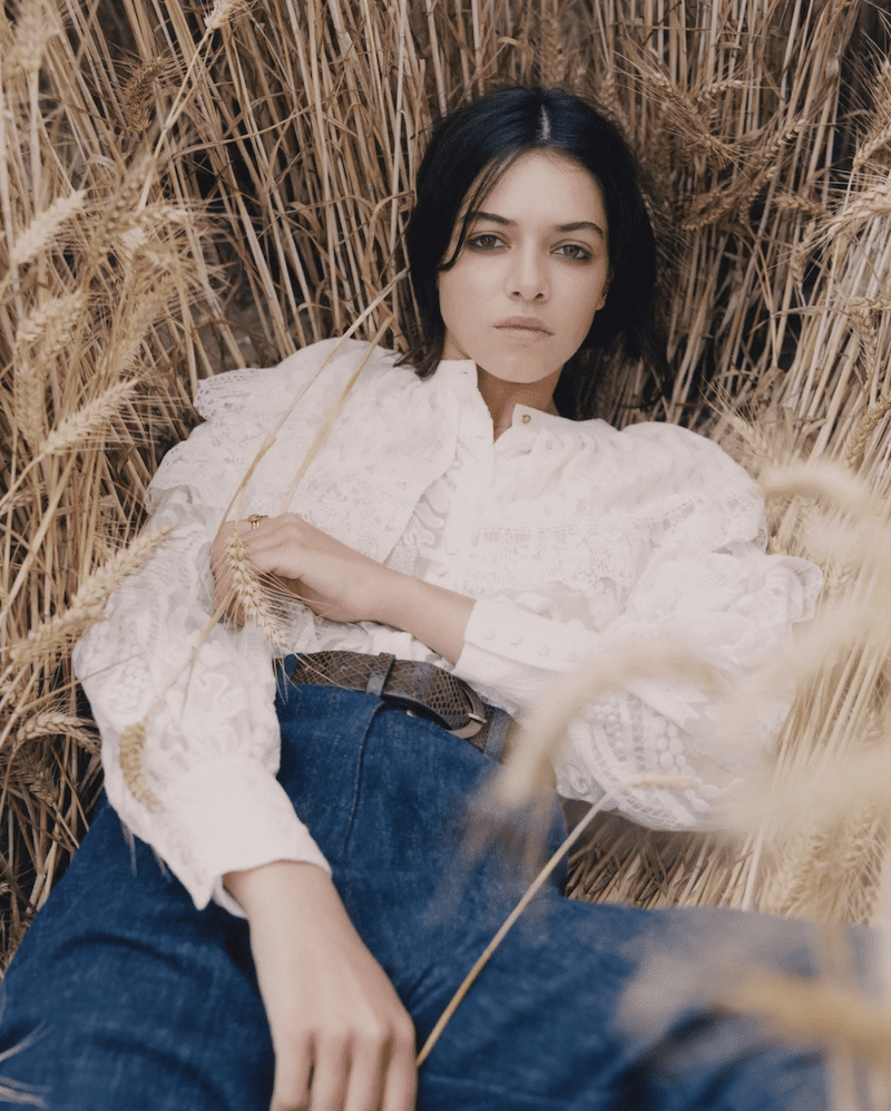 girl laying in wheat in jeans and a ruffly shirt