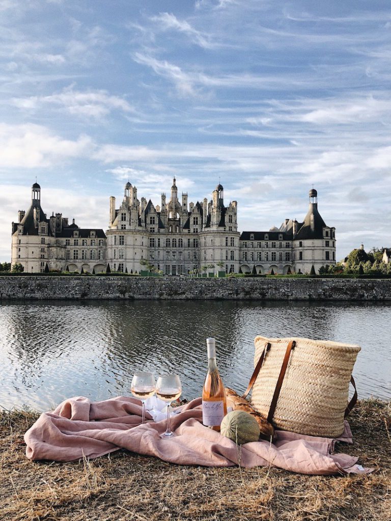 a bottle of rose and basket in front of a french chateau
