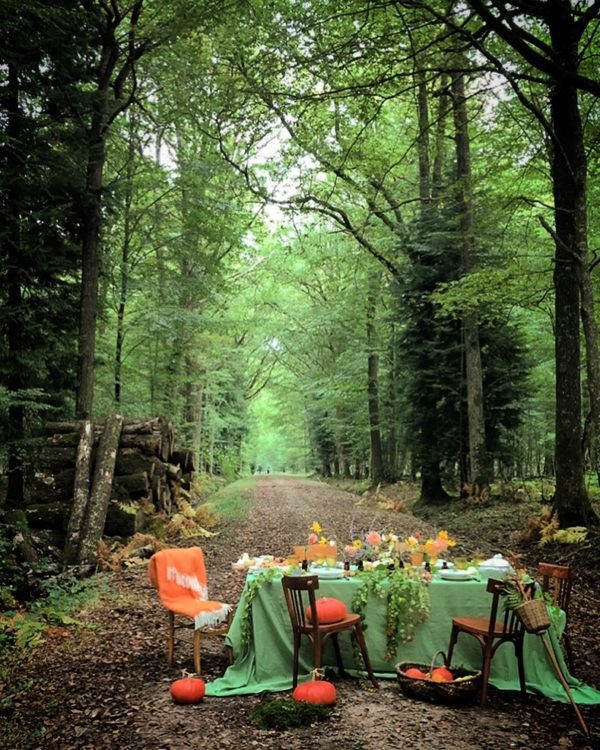 tablescape with green table cloth and orange chairs set up in a forest