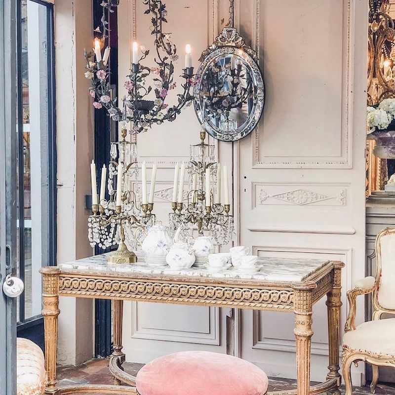 a gilded table, chandelier and pink velvet pouffe