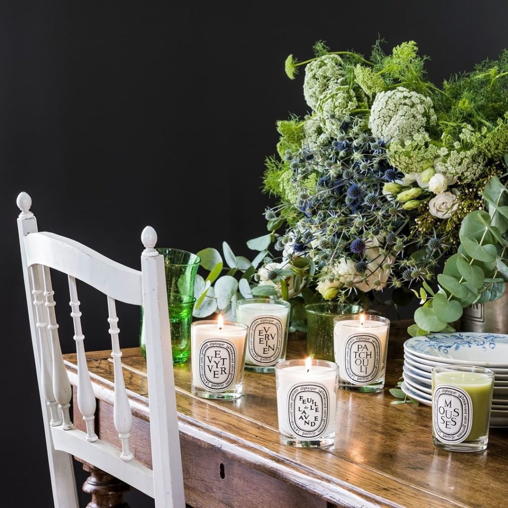 Collection of Diptyque candles on table with floral centerpiece.