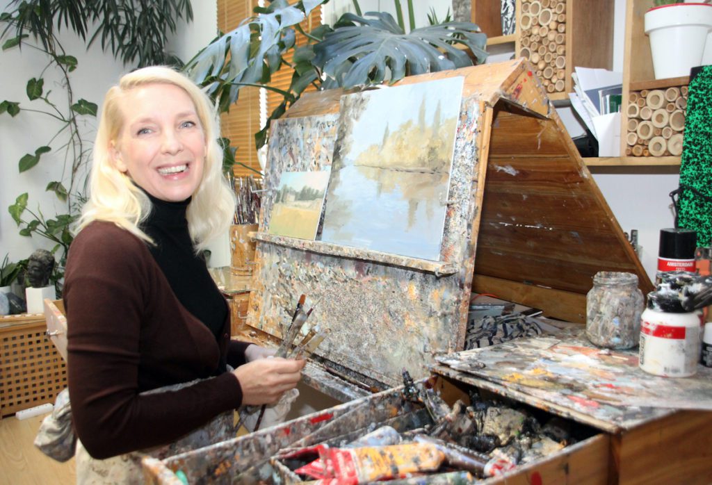 blonde female artist in front of painting