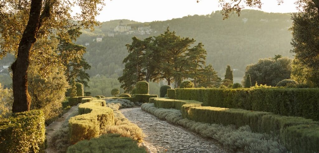 Perigord garden in Dordogne, France with lush hedges and a stone walking path with green mountains beyond.