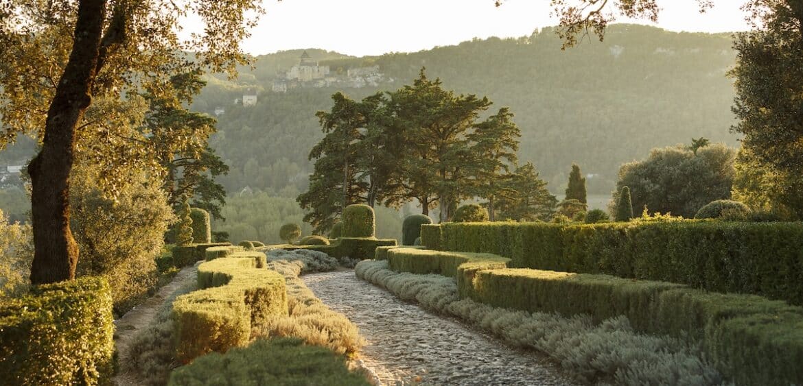 Perigord garden in Dordogne, France with lush hedges and a stone walking path with green mountains beyond.