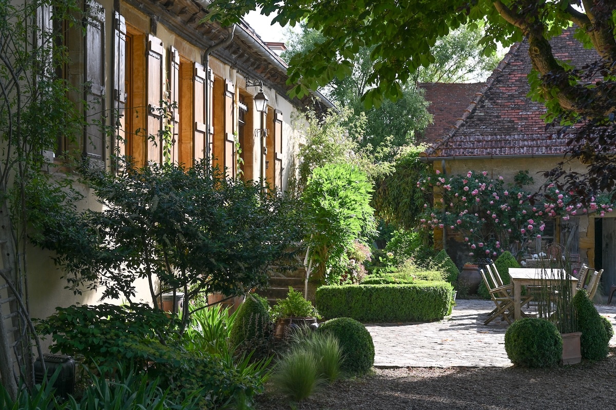 Garden courtyard and terrace with a rustic outdoor dining table and sunny home exterior in France.