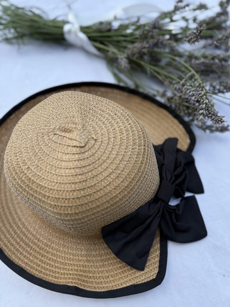 Straw hat with a black bow and lining styled beside freshly cut lavender flowers.