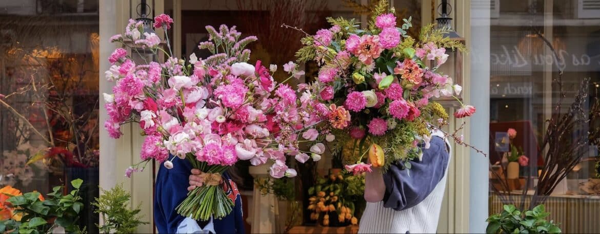 Large pink floral bouquets held outside of a Parisian flower shop.