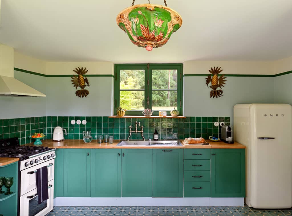 French kitchen interior with green cabinets and tiles, wood counter tops, and a unique antique light fixture.