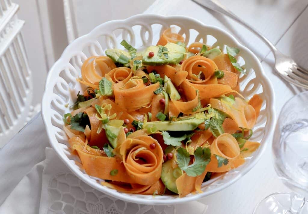 Ribboned carrot salad with avocado, mint, and parsley in a white ceramic serving bowl.