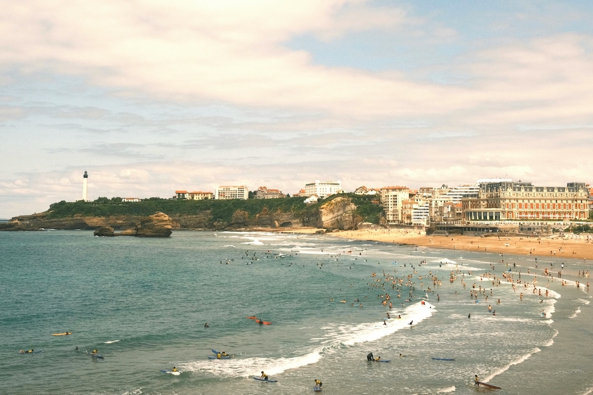 Crowded French beach with surfers and swimmers along the shallow parts of the shore.