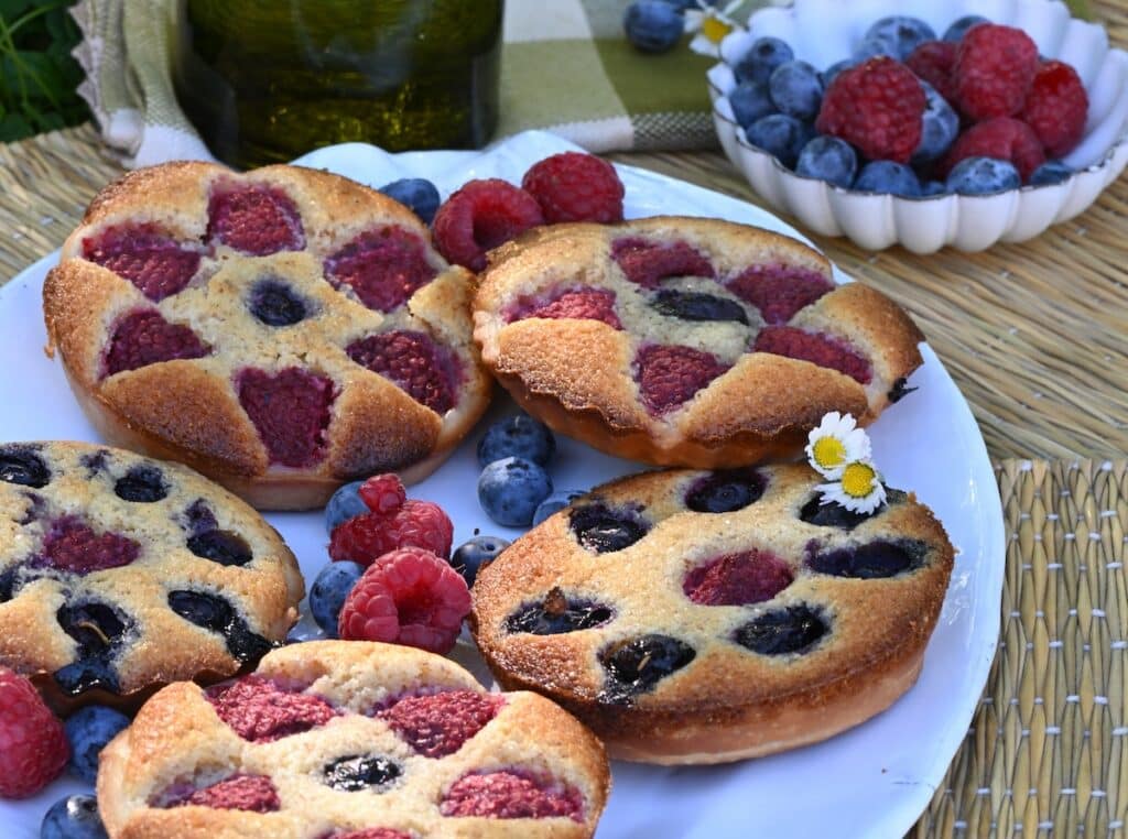 Plate of berry almond tartlets styled on a wicker picnic blanket.