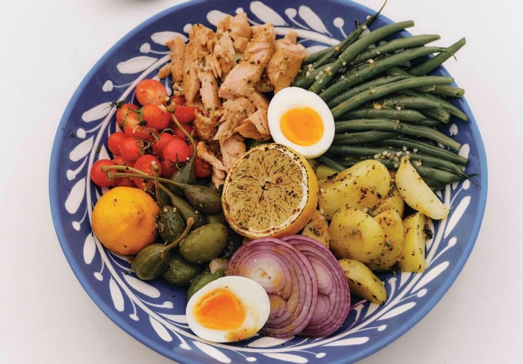 Niçoise salad arranged in a blue and white ceramic bowl.