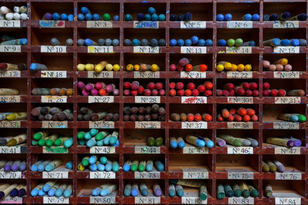 Colorful oil pastels arranged on a wood art organizer.