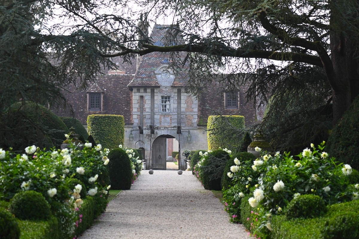A French chateau garden and walking path lined with lush white rose bushes.
