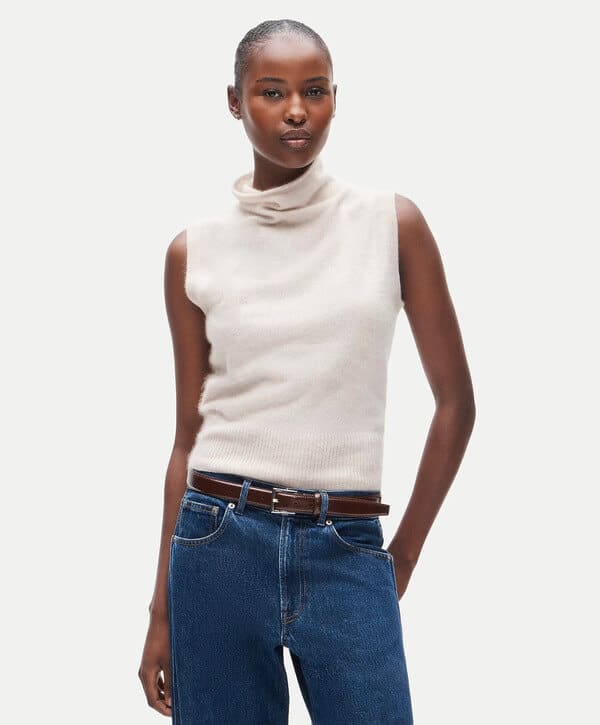 Cream cashmere sleeveless knit styled with a brown leather belt and blue jeans.
