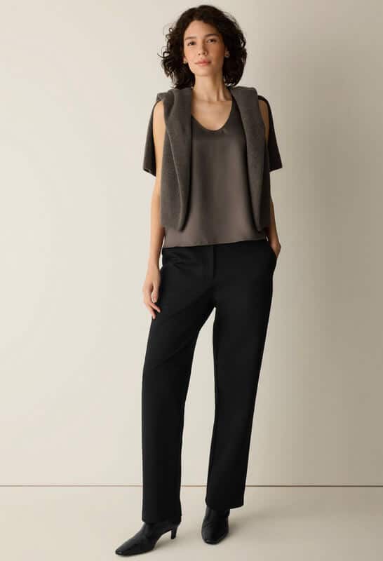 Cashmere and cotton blend Eileen Fisher knit sweater styled over the shoulders with black trousers and heeled boots.
