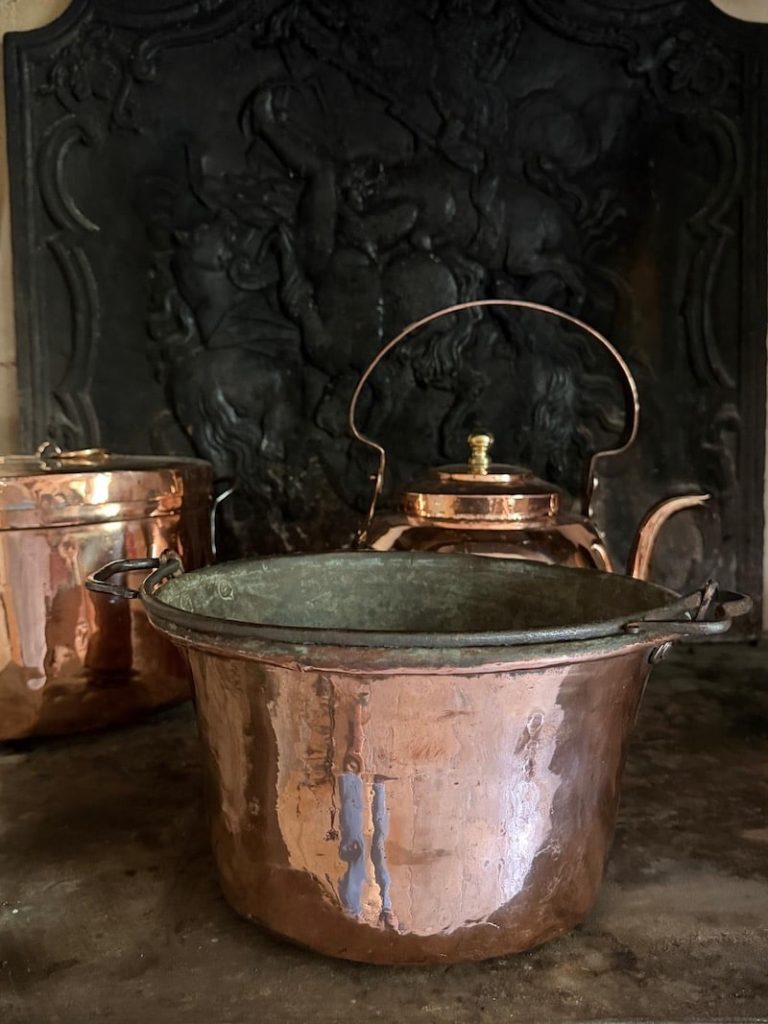 Vintage copper jam pan with iron handles beside a copper kettle and covered pot.