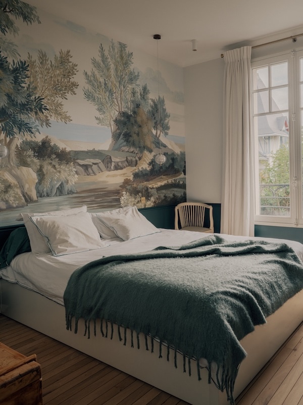 Bedroom interior featuring detailed wallpaper, a made bed, and soft natural light.