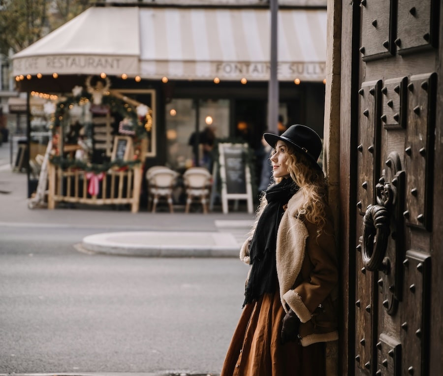 Woman in a shearling jacket and hat beside an ornate wooden door in Paris.